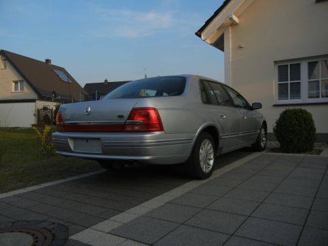 1999 Ford Fairlane - A silver sedan is parked on a paved driveway in front of a residential building.