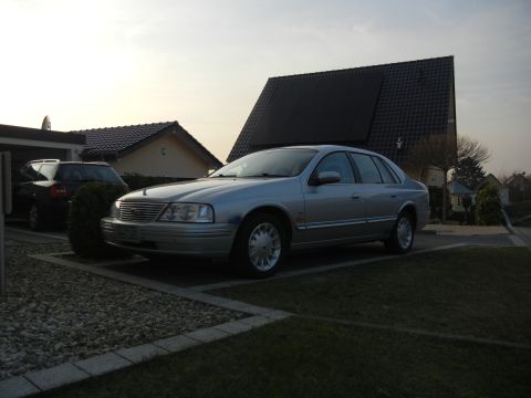 1999 Ford Fairlane - A silver sedan is parked in a residential driveway, with another vehicle visible in the garage.