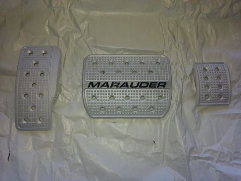 2003 Mercury Marauder - Three silver pedal covers are laid out on a white surface. One of the covers has the word MARAUDER embossed on it.