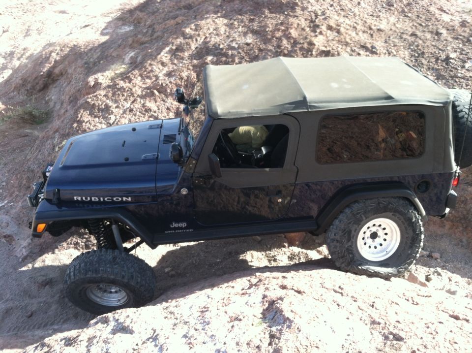 Dark blue Jeep Wrangler Rubicon Unlimited on rocky terrain. Has a soft top and spare tire on the back