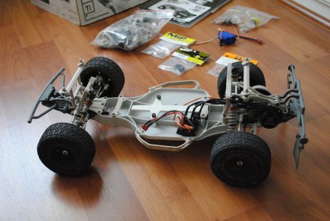 1986 Ford Bronco - A disassembled radio-controlled car chassis sits on a wooden floor surrounded by parts and packaging.