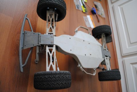 1986 Ford Bronco - The underside of an RC car chassis is shown, with various parts and tools visible on the wall in the background.