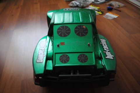 1986 Ford Bronco - A green remote control car body with racing decals sits on a wooden floor, with various parts scattered in the background.