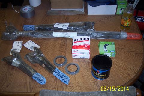 1973 Ford F-250 - Spicer front axle components, including knuckle joints and drive shafts, along with grease and oil seals, are laid out on a wooden table.