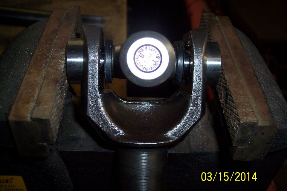 Close-up of a universal joint held in a vise. It has a circular marking with letters and numbers