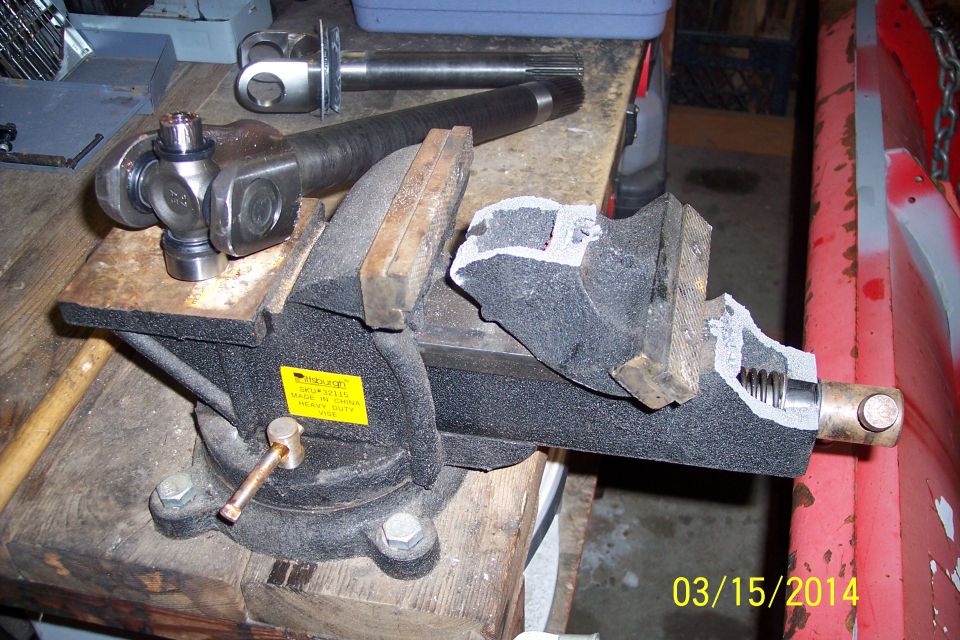 Driveshaft universal joint clamped in a vise, with another driveshaft in background
