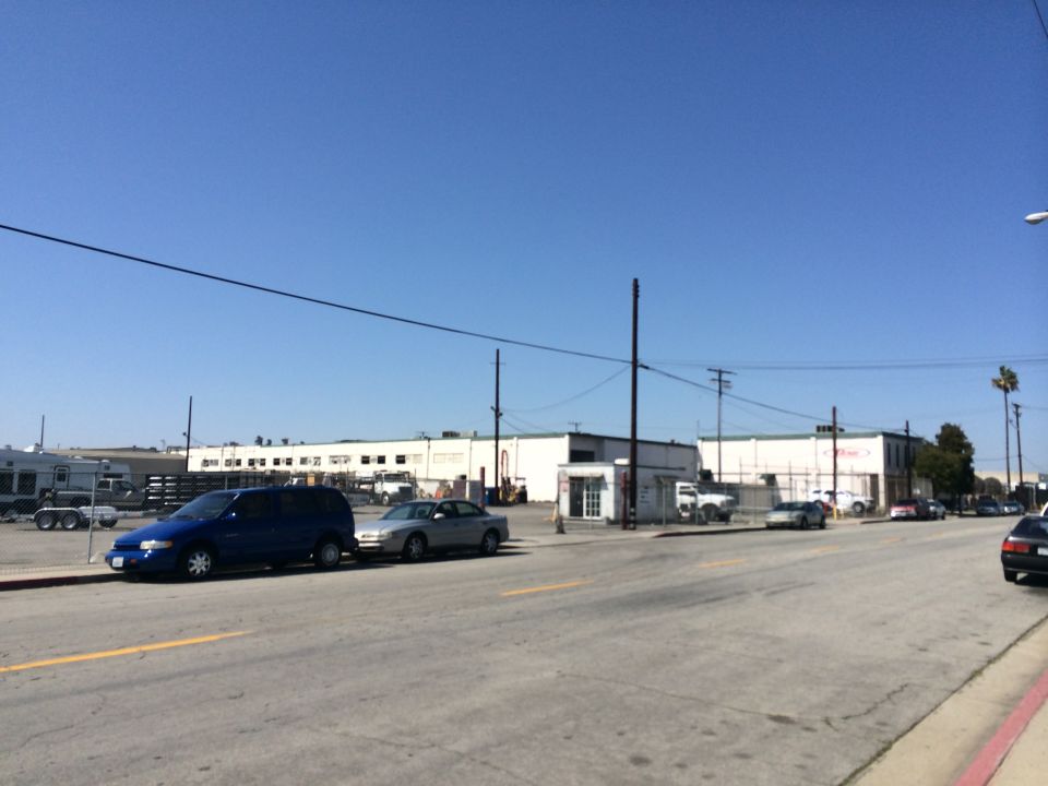 Blue minivan and silver sedan parked on a street in front of industrial buildings