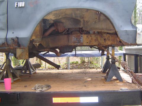 1986 Ford Bronco - Rusted F100 truck frame and suspension components are supported by jack stands on a trailer.