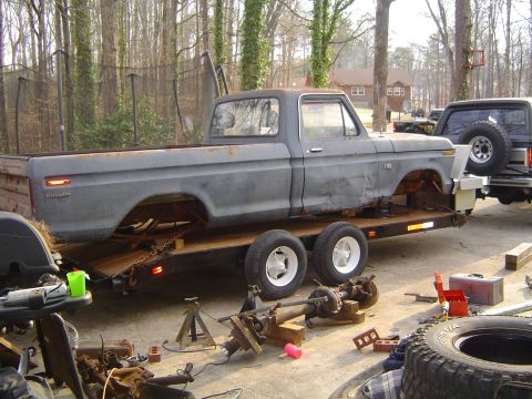 1986 Ford Bronco - A disassembled Ford pickup truck is being transported on a trailer, with various automotive parts nearby.