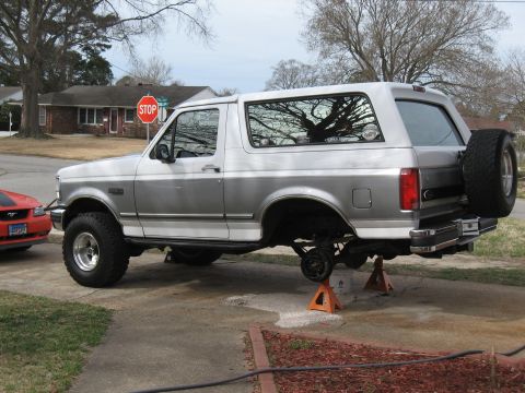 1994 Ford Bronco - Silver and gray Ford Bronco on jack stands with rear wheels removed, spare tire mounted on the tailgate.