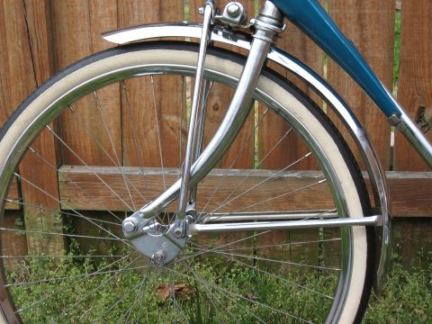1994 Ford Bronco - Close-up view of a bicycle's front wheel, chrome fork, and fender with a wooden fence in the background.