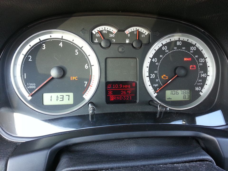Car dashboard with speedometer, tachometer, fuel gauge, temperature gauge, and digital display showing time, MPG, temperature, and gear