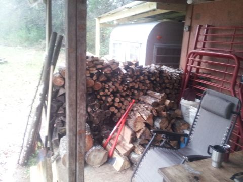 1986 Ford Bronco - A covered porch area holds a large pile of firewood, a small trailer, and outdoor furniture.