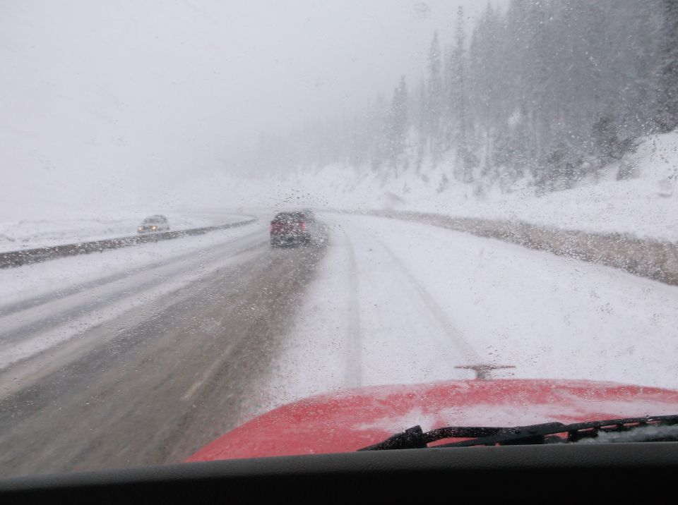 View from inside a vehicle driving on a snow-covered highway with other cars ahead