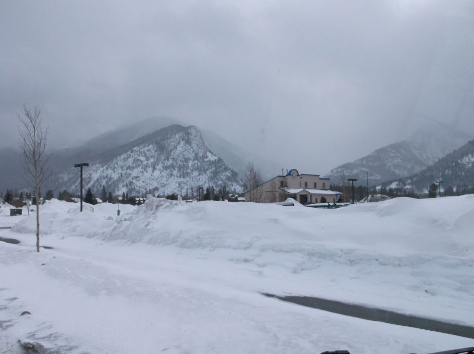 Snow-covered ground and mountains under a cloudy sky, with a building in the mid-ground