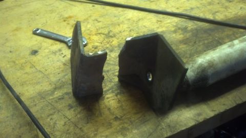 1995 Ford Bronco - A metal part, possibly a shock mount, is broken into two pieces on a workbench.