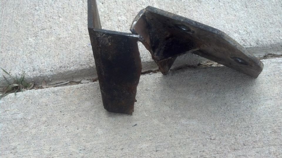 Two rusted metal brackets, one L-shaped and one with triangular protrusions, lying on a concrete surface