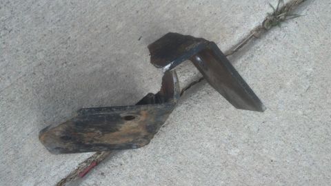 1995 Ford Bronco - A damaged metal bracket lies on a concrete surface, possibly a vehicle part.