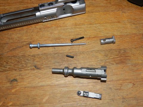 1996 Ford Bronco - Disassembled rifle parts, including the bolt carrier group and firing pin, are laid out on a wooden surface.