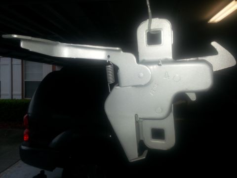 1994 Ford Bronco - A close-up of a vehicle's hood latch mechanism, with a dark SUV in the background.