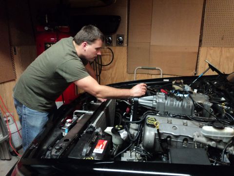 2004 Mercury Grand Marquis - A person works on a vehicle's engine bay, which features a prominent supercharger.