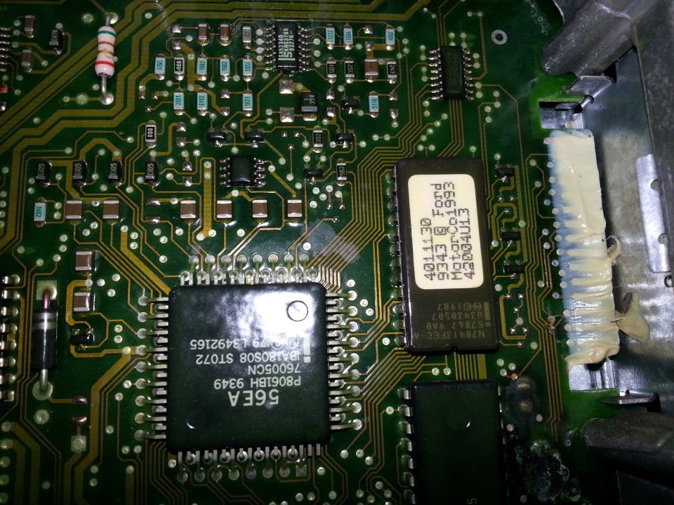Close-up of a green circuit board with black and white chips, wires, and resistors. Text on one chip reads 'Ford'