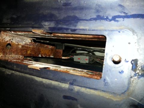 1994 Ford Bronco - Detail of rusted metal and wiring harness visible through an opening in a blue vehicle.
