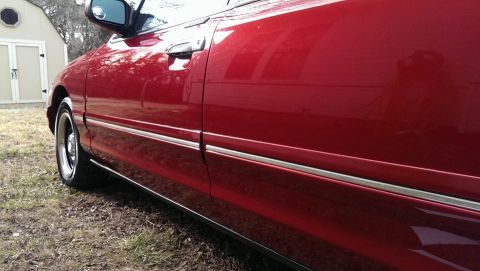 2000 Mercury Grand Marquis - A red sedan is viewed from the side, with a reflection visible on its door.