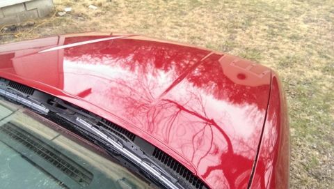 2000 Mercury Grand Marquis - The hood of a red car shows reflections of the surrounding environment, including trees and a building.