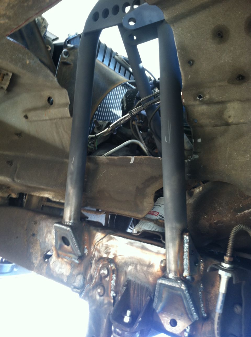 Custom fabricated front suspension components welded to a rusty frame, with a radiator visible behind