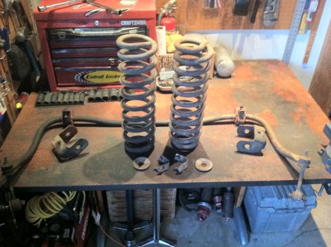 1977 Ford F-350 - Front coil springs and sway bar components are laid out on a workbench with tools and a red toolbox in the background.