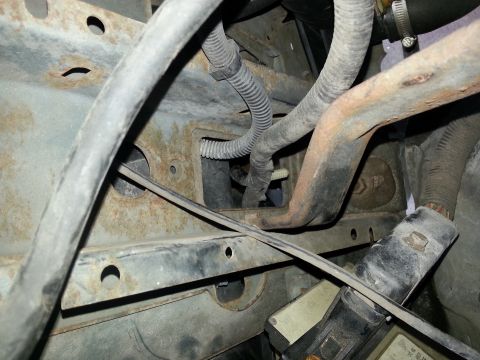 1994 Ford Bronco - Close-up view of hoses and rusted metal components within a vehicle's engine bay.