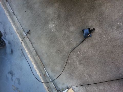 1994 Ford Bronco - A detached hood latch cable and mechanism lies on a concrete surface.
