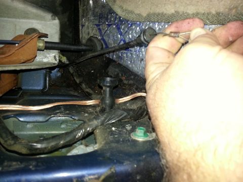 1994 Ford Bronco - Close-up of a hand adjusting a cable release mechanism, likely for a hood or trunk, within a vehicle's interior or undercarriage.