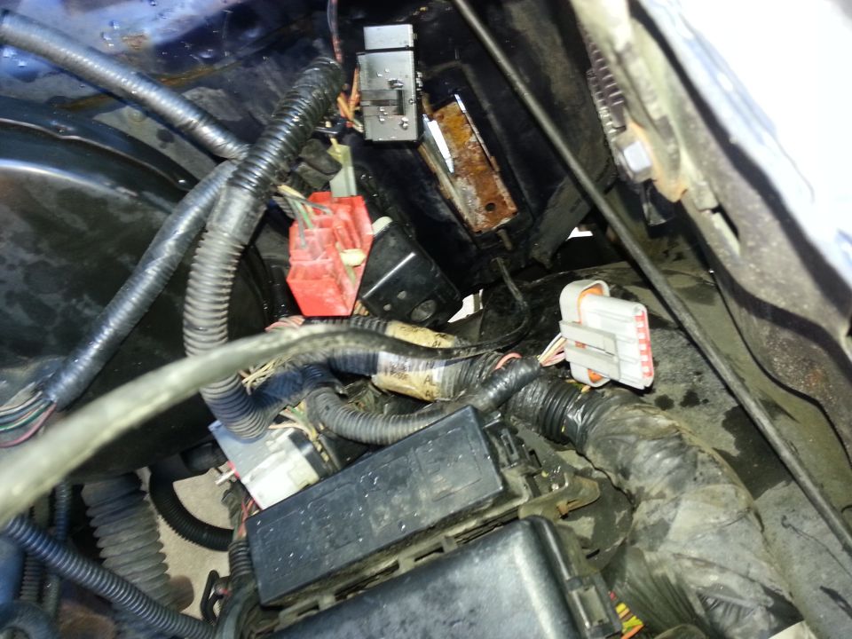 Close-up of a vehicle's engine bay wiring, showing connectors, a fuse box, and various cables