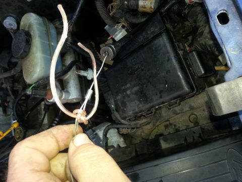 1994 Ford Bronco - A hand manipulates wires in the engine bay of a blue vehicle, near the fuse box and brake fluid reservoir.