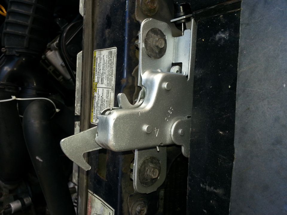 Close-up of a vehicle's hood latch mechanism and surrounding engine components