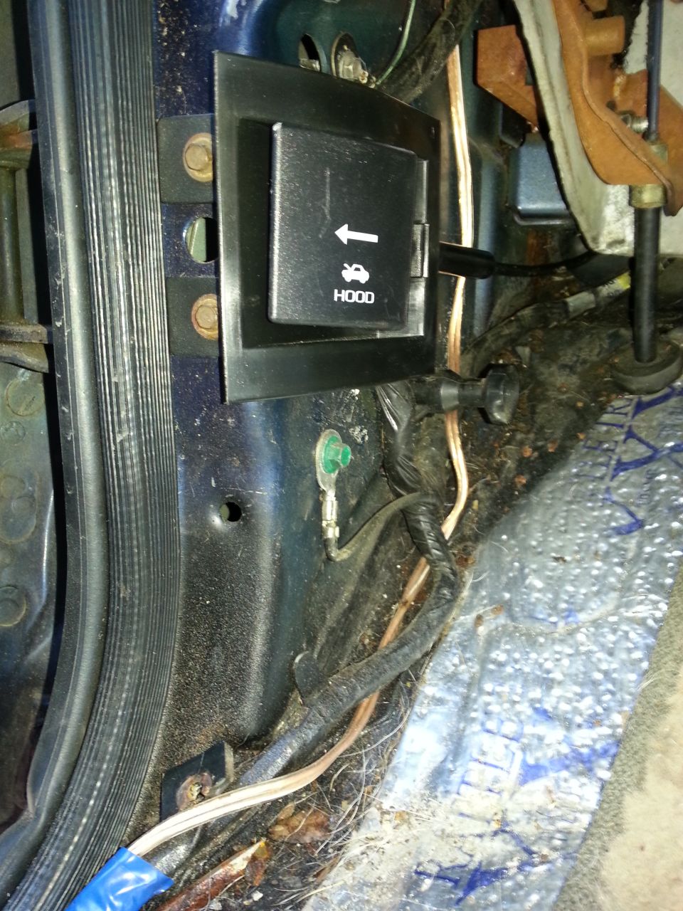 Interior view of a car's hood release lever with "HOOD" text and an upward arrow icon