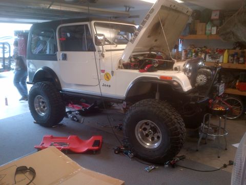 1985 Jeep CJ7 - A white 1985 Jeep CJ7 Laredo is parked in a garage with its hood open, showing the engine compartment.