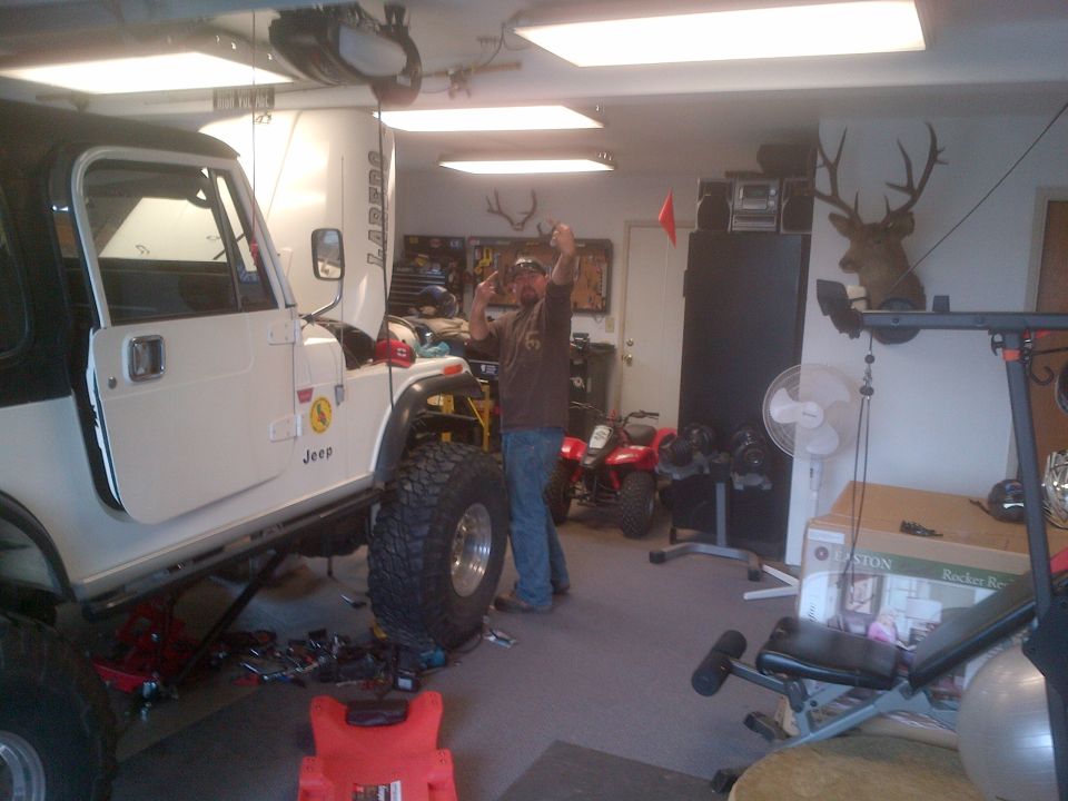 White 1985 Jeep CJ7 with black top, lifted suspension, and large tires in a garage. A person stands next to it