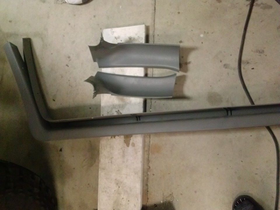 Gray plastic trim pieces for a car door, one long piece and two curved sections, resting on concrete