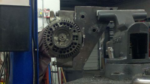 1989 Ford F-150 - An alternator is secured in a vise, attached to a metal plate, with a blue lift visible on the side.