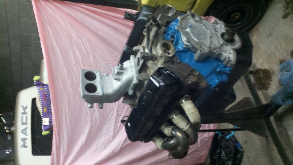 Engine on a stand, partially covered by a pink tarp. Text on a white surface behind it reads 'MACK'