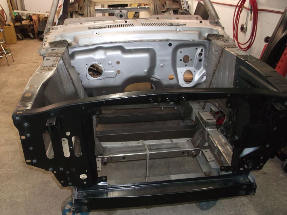 Car chassis on a dolly, showing the engine bay and front frame. The body is partially stripped