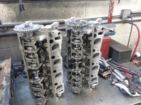 2004 Ford Crown Victoria - Two engine cylinder heads are displayed on a workbench, showing internal components and gears.