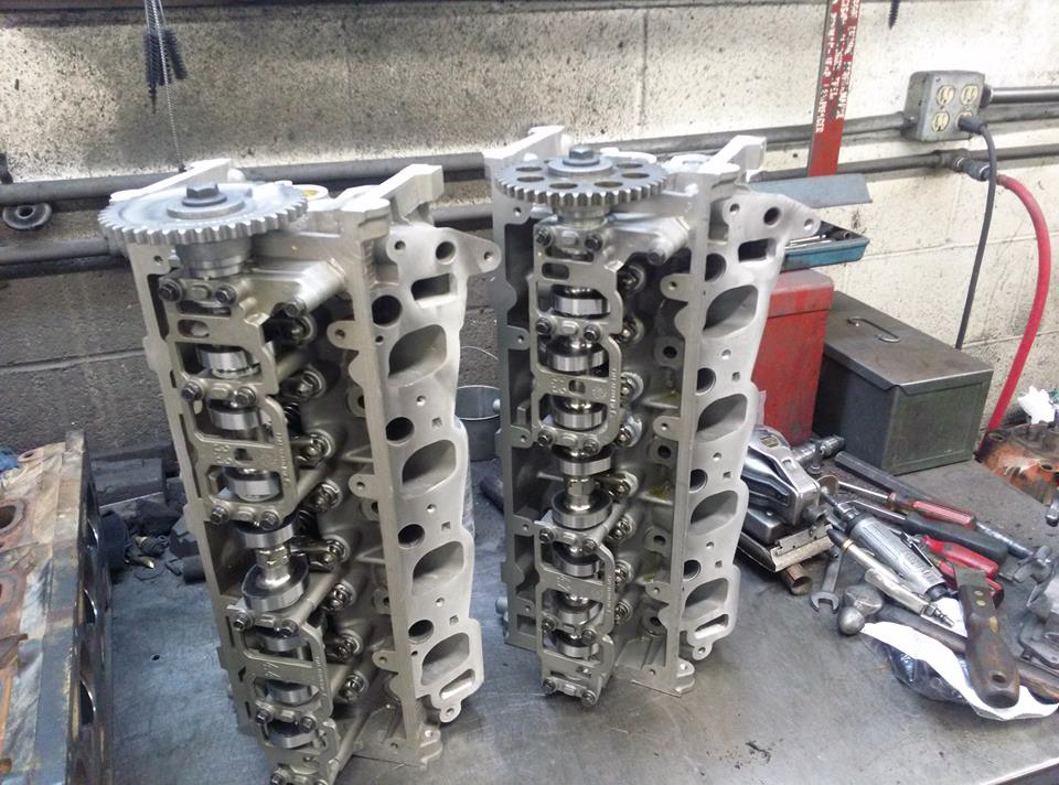 Pair of rebuilt aluminum SOHC cylinder heads with cam sprockets on a workbench
