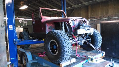 1985 Jeep CJ7 - This modified Jeep is on a trailer, being worked on in a garage with a vehicle lift.