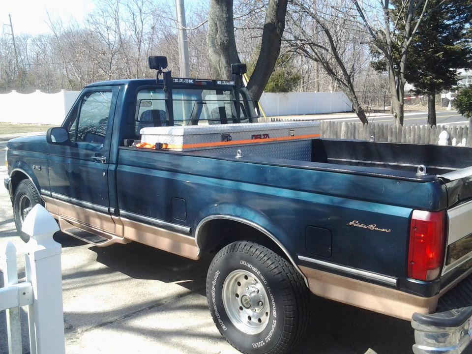 Dark green and tan pickup truck, rear three-quarter view, with toolbox and headache rack in bed
