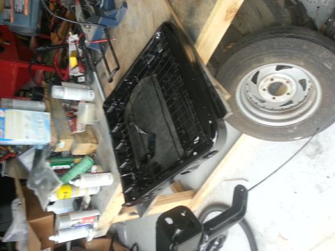 1994 Ford Bronco - A black vehicle seat frame is shown disassembled and resting on wooden supports in a cluttered garage.