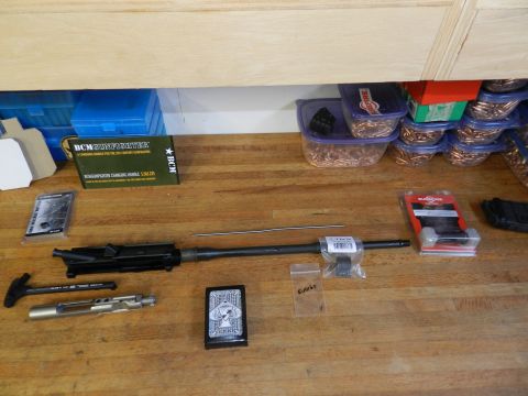 1996 Ford Bronco - Various firearm components, including a bolt carrier group and charging handle, are laid out with ammunition on a wooden workbench.